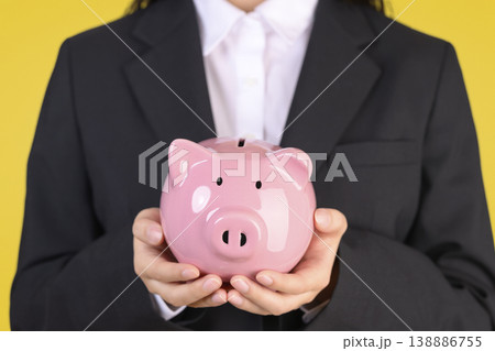 豚の貯金箱を持つスーツを着た女性 豚の貯金箱を持つスーツを着た女性 138886755
