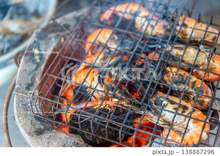 Fresh prawns grilling over charcoal fire with smoky heat glowing embers and rustic metal grate capturing rich seafood texture and outdoor cooking atmosphere appetizing detail 138887296
