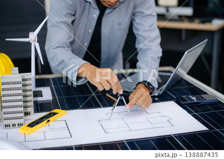 Architect planning eco-friendly building with wind turbine model, blueprints, and laptop. Ideal for green energy, smart city, Architect planning eco-friendly building with wind turbine model, blueprints, and laptop. Ideal for green energy, smart city, 138887435
