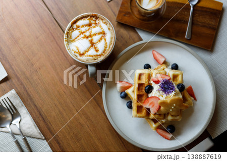 Cup of hot milk caramel macchiato coffee and plate of waffles on table by the window. Cup of hot milk caramel macchiato coffee and plate of waffles on table by the window. 138887619
