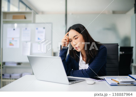 Asian businesswoman showing stress and frustration at office desk with laptop and calculator. Real people, financial pressure, work overload, deadline stress, burnout concept. Asian businesswoman showing stress and frustration at office desk with laptop and calculator. Real people, financial pressure, work overload, deadline stress, burnout concept. 138887964