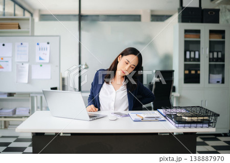 Asian businesswoman stretching arms in office with tired expression, relieving muscle tension from long work hours. Asian businesswoman stretching arms in office with tired expression, relieving muscle tension from long work hours. 138887970