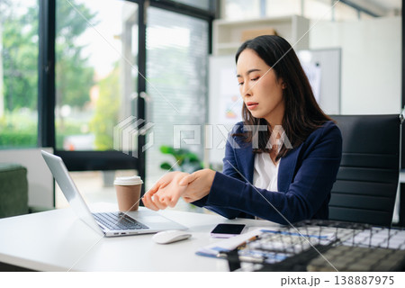 Asian businesswoman stretching arms in office with tired expression, relieving muscle tension from long work hours. Asian businesswoman stretching arms in office with tired expression, relieving muscle tension from long work hours. 138887975