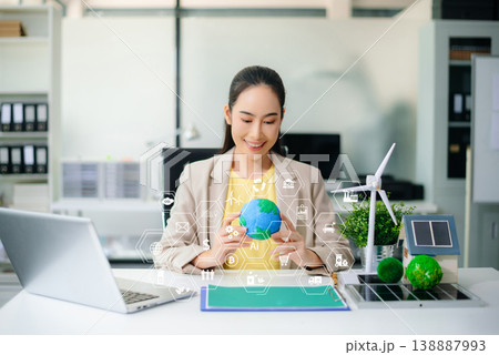 Hands holding Earth globe with futuristic clean energy icons overlay. Sustainability, smart technology, battery, wind, solar, and eco-friendly innovation concept in office. 138887993