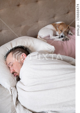 Man sleeping in bed with his puppy. Tired guy taking nap with domestic pet on soft pillow. Man sleeping in bed with his puppy. Tired guy taking nap with domestic pet on soft pillow. 138888474