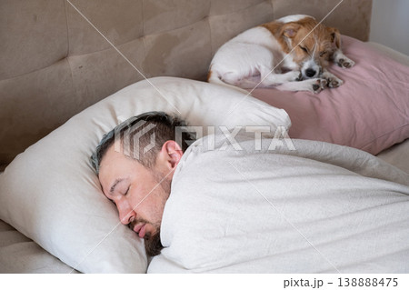 Man sleeping in bed at home with his small dog. Caucasian guy resting on pillow next to pet puppy. Man sleeping in bed at home with his small dog. Caucasian guy resting on pillow next to pet puppy. 138888475