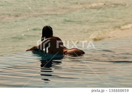 A beautiful tanned girl with an athletic physique in a swimsuit is at the edge of the pool of the villa pool on a sunset in the Maldives, she is happy and posing 138888659
