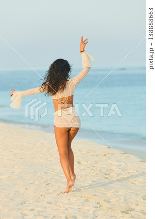 A beautiful tanned girl in a swimsuit runs along a white beach at sunset in the Maldives, she is happy, posing for a photographer A beautiful tanned girl in a swimsuit runs along a white beach at sunset in the Maldives, she is happy, posing for a photographer 138888663
