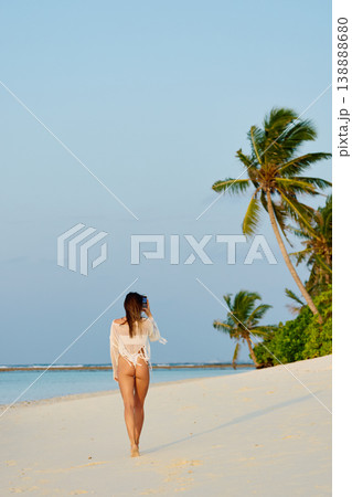 A beautiful tanned girl in a swimsuit walks along a white beach at sunset in the Maldives, she is happy, posing for a photographer 138888680