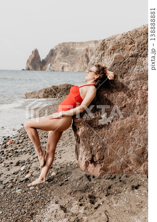 Woman swimsuit beach leaning against rock in red swimwear on pebble shore with ocean waves during summer vacation 138888881