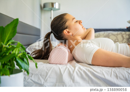 Woman positioning head on ergonomic orthopedic pillow for proper cervical spine support. Adjusting neck alignment before sleep to reduce pain, relieve tension and improve posture and sleep quality. 138890058