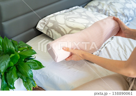 Woman holding ergonomic orthopedic pillow near bed preparing for sleep. Cervical spine support for proper neck alignment, posture correction and relief from tension, discomfort and muscle stiffness. Woman holding ergonomic orthopedic pillow near bed preparing for sleep. Cervical spine support for proper neck alignment, posture correction and relief from tension, discomfort and muscle stiffness. 138890061
