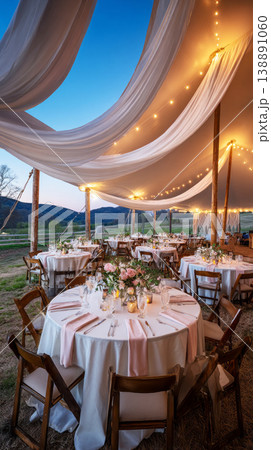 An outdoor wedding tent showcases macrame details and soft floral arrangements. Tables are set for guests with candles, bringing a warm glow as evening approaches at the venue 138891060