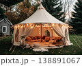 A wedding tent is set up in a grassy space with trees around. Inside, there are cushions and lights creating a cozy atmosphere for guests to relax and enjoy 138891067