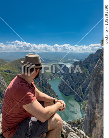 A man tourist is sitting on a rock on the background of a mountain river A man tourist is sitting on a rock on the background of a mountain river 138891890