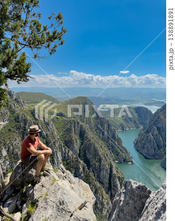 A man tourist is sitting on a rock on the background of a mountain river A man tourist is sitting on a rock on the background of a mountain river 138891891