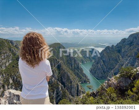 Hiker woman on the background of a mountain river. Girl traveler stands on the edge of rock Hiker woman on the background of a mountain river. Girl traveler stands on the edge of rock 138892001