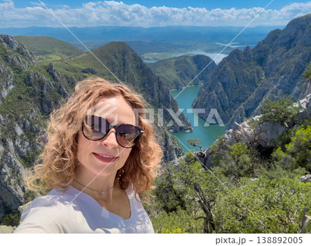 Hiker woman on the background of a mountain river. Girl traveler stands on the edge of rock 138892005