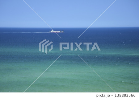 青色と緑色が重なり合う海の水平線近くを一隻の船が左から右に航行して青空の広がる風景 138892366