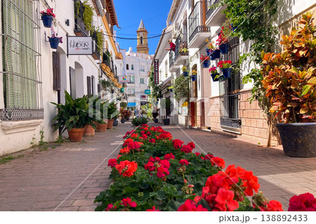 A bright white street lined with colorful flower pots and blooming plants creates a charming Mediterranean scene in Estepona, Spain 138892433