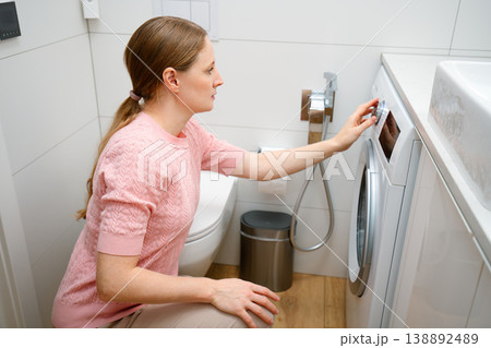 A young woman turns on a washing machine A young woman turns on a washing machine 138892489