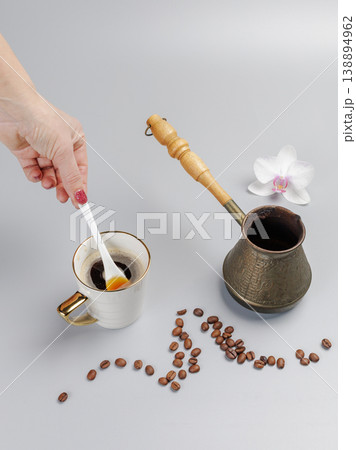 Woman's hand with a cup of coffee. Cezve with roasted coffee beans and an orchid flower. 138894962