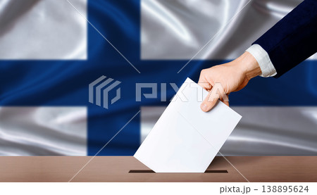 Finland Parliamentary vote 2026. Hand placing a ballot in ballot box with the Finnish flag in the background Finland Parliamentary vote 2026. Hand placing a ballot in ballot box with the Finnish flag in the background 138895624