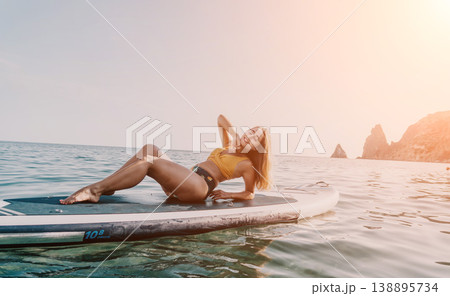 Woman Paddleboard Beach Relaxing: Young woman in a swimsuit relaxing on a paddleboard in the ocean near a beach. Woman Paddleboard Beach Relaxing: Young woman in a swimsuit relaxing on a paddleboard in the ocean near a beach. 138895734