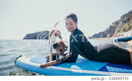 Woman Dog Paddleboard Beach - Woman and dog paddleboarding together on a blue paddleboard in the sea. Woman Dog Paddleboard Beach - Woman and dog paddleboarding together on a blue paddleboard in the sea. 138895735