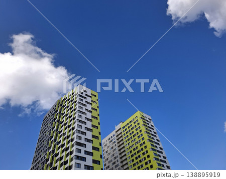 Bright modern apartment buildings stand tall under a clear blue sky. Fluffy clouds move gently above the colorful structures in an urban setting during daytime. Bright modern apartment buildings stand tall under a clear blue sky. Fluffy clouds move gently above the colorful structures in an urban setting during daytime. 138895919