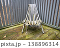 Folded wooden deck chair on weathered terrace with gray fence and rustic outdoor texture 138896314