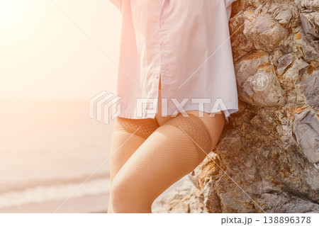 Stockings hosiery beach woman wearing light shirt leans on coastal rock during golden hour sunset Stockings hosiery beach woman wearing light shirt leans on coastal rock during golden hour sunset 138896378
