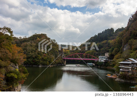 秋の渓谷と湖に架かる赤い橋と遊覧船の航跡が広がる静かな水面風景（日本の自然・観光地イメージ） 138896443