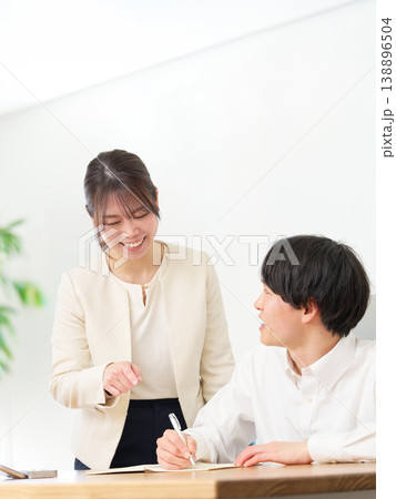 スーツ姿の女性に教わりながらノートを取る若い男性 スーツ姿の女性に教わりながらノートを取る若い男性 138896504