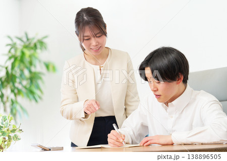 スーツ姿の女性に教わりながら学習する若い男性 スーツ姿の女性に教わりながら学習する若い男性 138896505