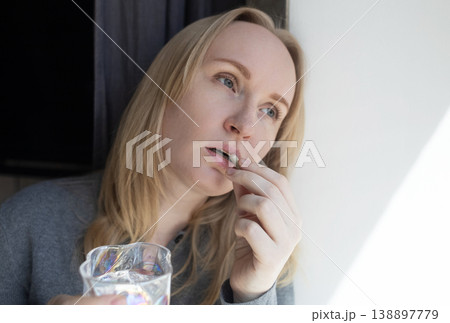 Woman taking iron supplement capsule with glass of water. Female health care, iron deficiency anemia treatment, vitamins and minerals intake for wellness. Woman taking iron supplement capsule with glass of water. Female health care, iron deficiency anemia treatment, vitamins and minerals intake for wellness. 138897779