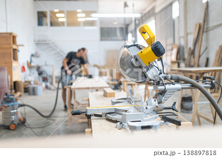 Miter saw on worktable with carpenter sanding wood Miter saw on worktable with carpenter sanding wood 138897818