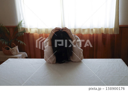 髪も整えず部屋着のまま力なく頭を抱える女性 髪も整えず部屋着のまま力なく頭を抱える女性 138900176