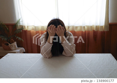 髪も整えず部屋着のまま力なくうつむく女性 138900177