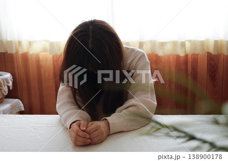 髪も整えず部屋着のまま力なくうつむく女性 138900178