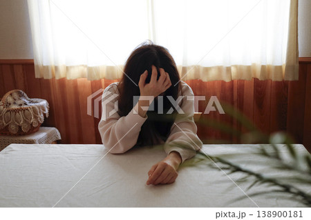 髪も整えず部屋着のまま力なくうつむく女性 髪も整えず部屋着のまま力なくうつむく女性 138900181