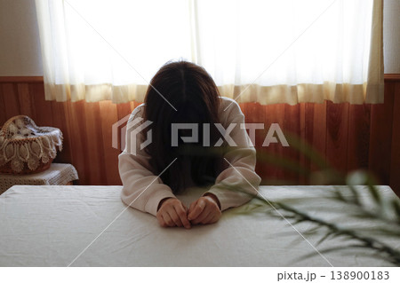 髪も整えず部屋着のまま力なくうつむく女性 138900183