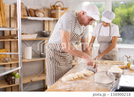 Elderly man and woman cutting and braiding dough 138900218