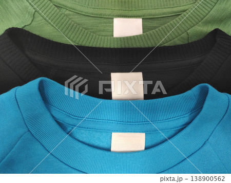 Three T-shirts black blue and green with Blank white label indicating clothing size and washing instructions 138900562