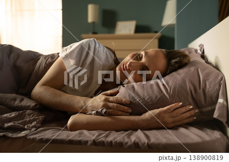 Young woman lying comfortably in bed, sleeping peacefully on a soft pillow while sunlight streams through the window, symbolizing rest, relaxation, and a fresh start to the day Young woman lying comfortably in bed, sleeping peacefully on a soft pillow while sunlight streams through the window, symbolizing rest, relaxation, and a fresh start to the day 138900819