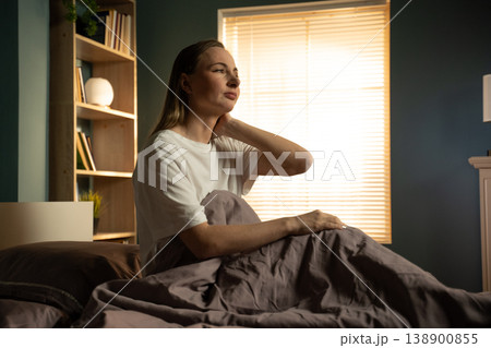 Woman wakes in morning, sits in bed rubbing her neck, wincing from stiffness and ache after poor sleep or bad posture, showing tension and morning discomfort Woman wakes in morning, sits in bed rubbing her neck, wincing from stiffness and ache after poor sleep or bad posture, showing tension and morning discomfort 138900855
