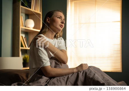 Woman sitting in bed, holding her shoulder in discomfort, feeling an injury or muscle ache after waking up, highlighting concepts of pain, exhaustion, and healthcare Woman sitting in bed, holding her shoulder in discomfort, feeling an injury or muscle ache after waking up, highlighting concepts of pain, exhaustion, and healthcare 138900864