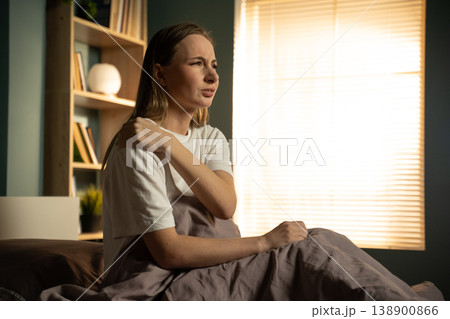 Woman sitting in bed, holding her painful shoulder, expressing discomfort and stiffness after waking up, showing musculoskeletal aches and health problems Woman sitting in bed, holding her painful shoulder, expressing discomfort and stiffness after waking up, showing musculoskeletal aches and health problems 138900866