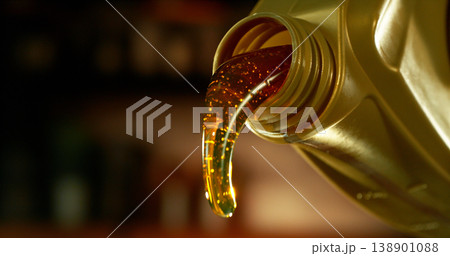 Close-up of motor oil pouring from a plastic container. Golden viscous liquid with bubbles flowing smoothly, automotive maintenance concept with shallow depth of field. Close-up of motor oil pouring from a plastic container. Golden viscous liquid with bubbles flowing smoothly, automotive maintenance concept with shallow depth of field. 138901088