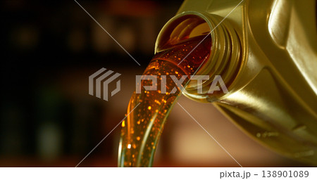 Close-up of motor oil pouring from a plastic container. Golden viscous liquid with bubbles flowing smoothly, automotive maintenance concept with shallow depth of field. Close-up of motor oil pouring from a plastic container. Golden viscous liquid with bubbles flowing smoothly, automotive maintenance concept with shallow depth of field. 138901089